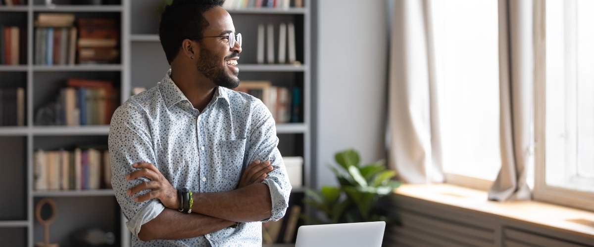 Young male business owner smiling while looking out office window.